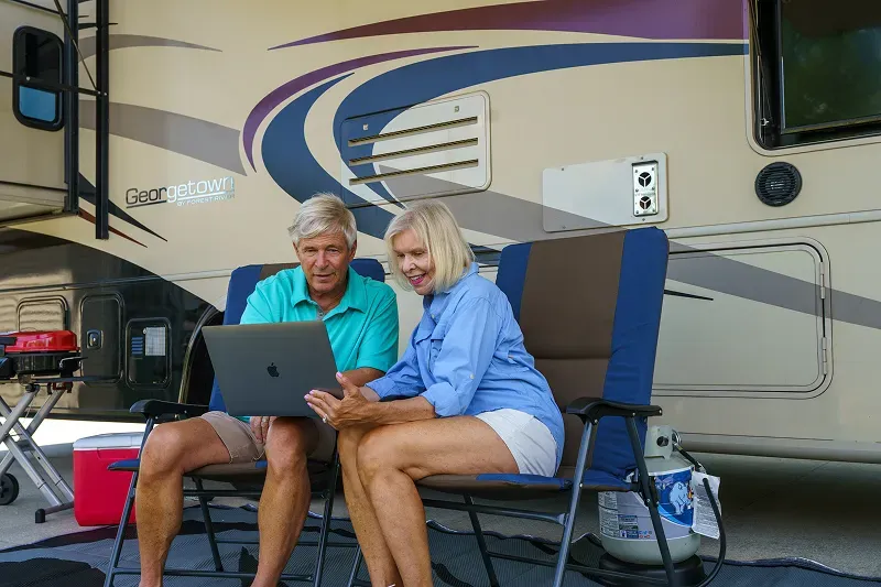 People sitting on chairs outside RV working on a computer