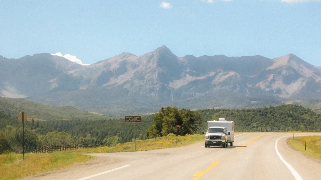 An RV droves down a road with large mountains in the background. 