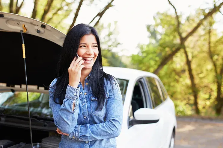 Woman in front of a car with the hood up on the phone