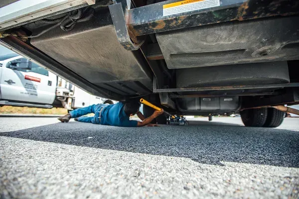 A technician is underneath a vehicle doing maintenance.