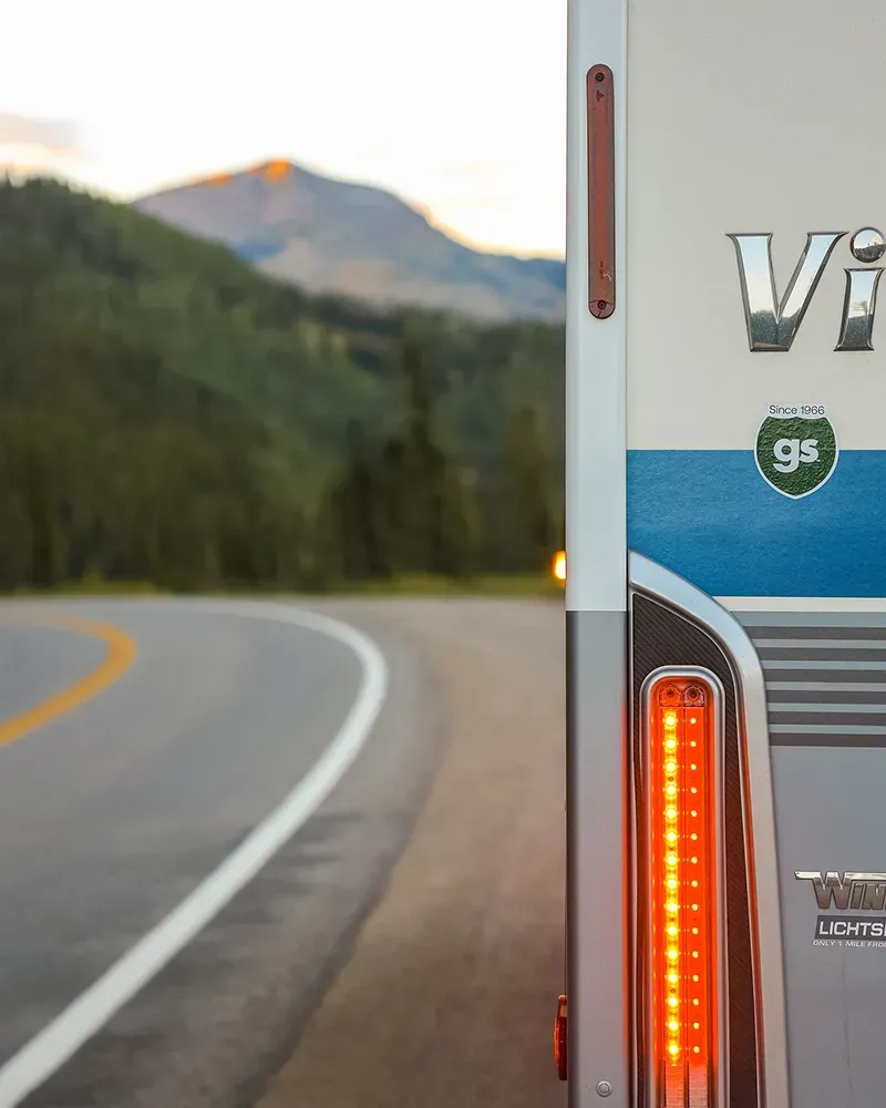 Close up image of an RV tail light on the side of the road with mountains ahead.