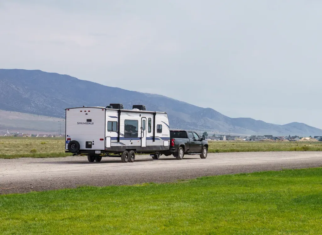 Travel trailer driving down a dirt road with mountains in the background