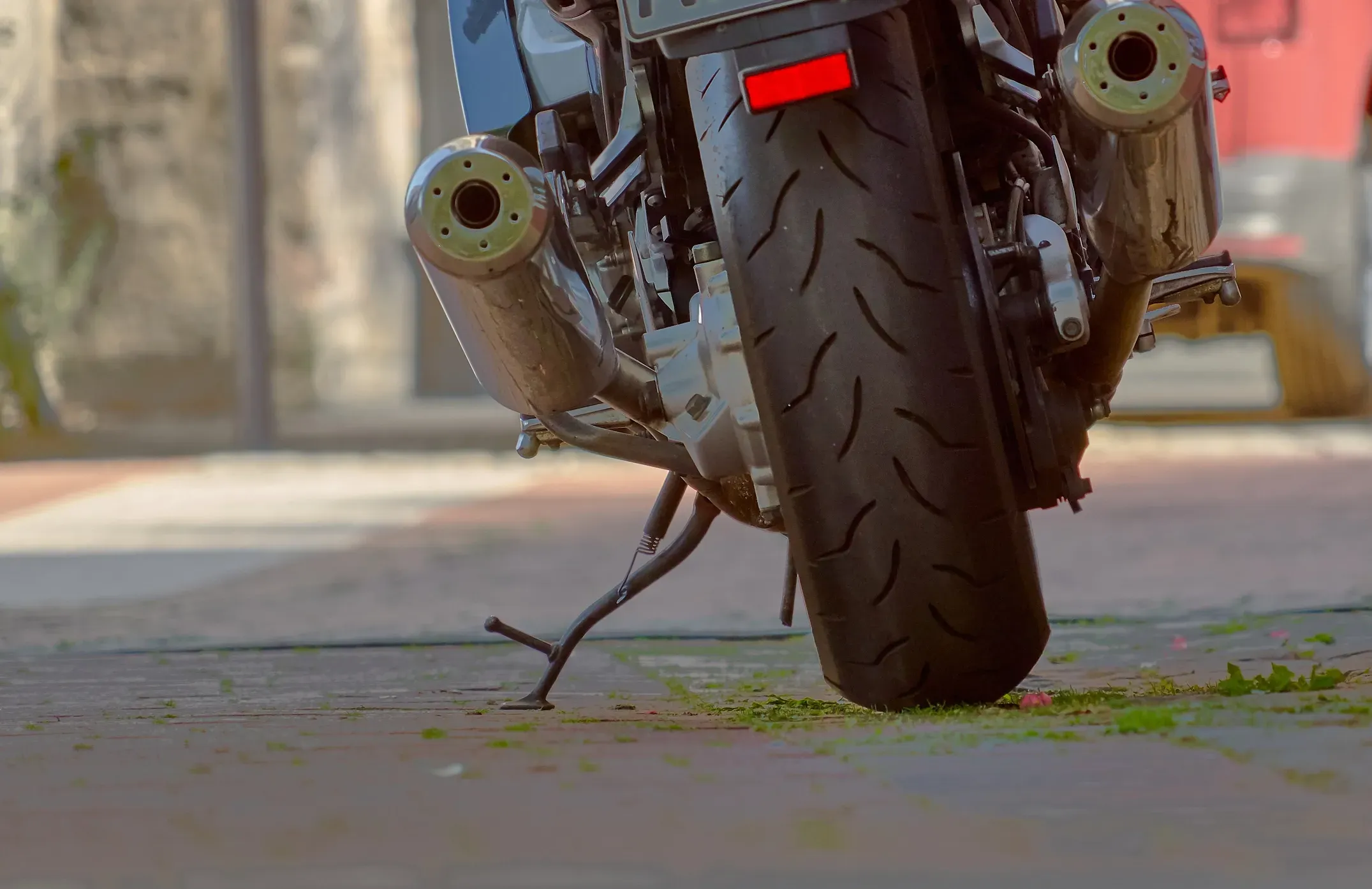 The rear view of a motorcycle including the rear tire, mufflers and kickstand.