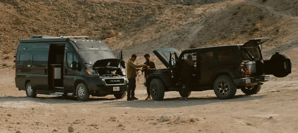 Two men in the desert using an off-road SUV to jumpstart a Class B RV