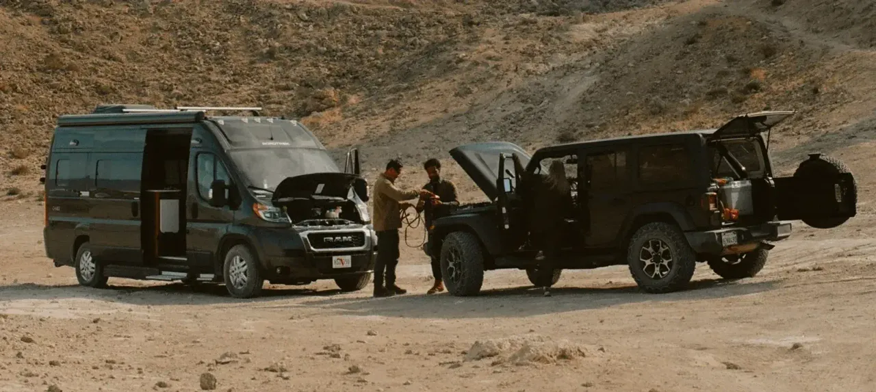 Two men in the desert using an off-road SUV to jumpstart a Class B RV