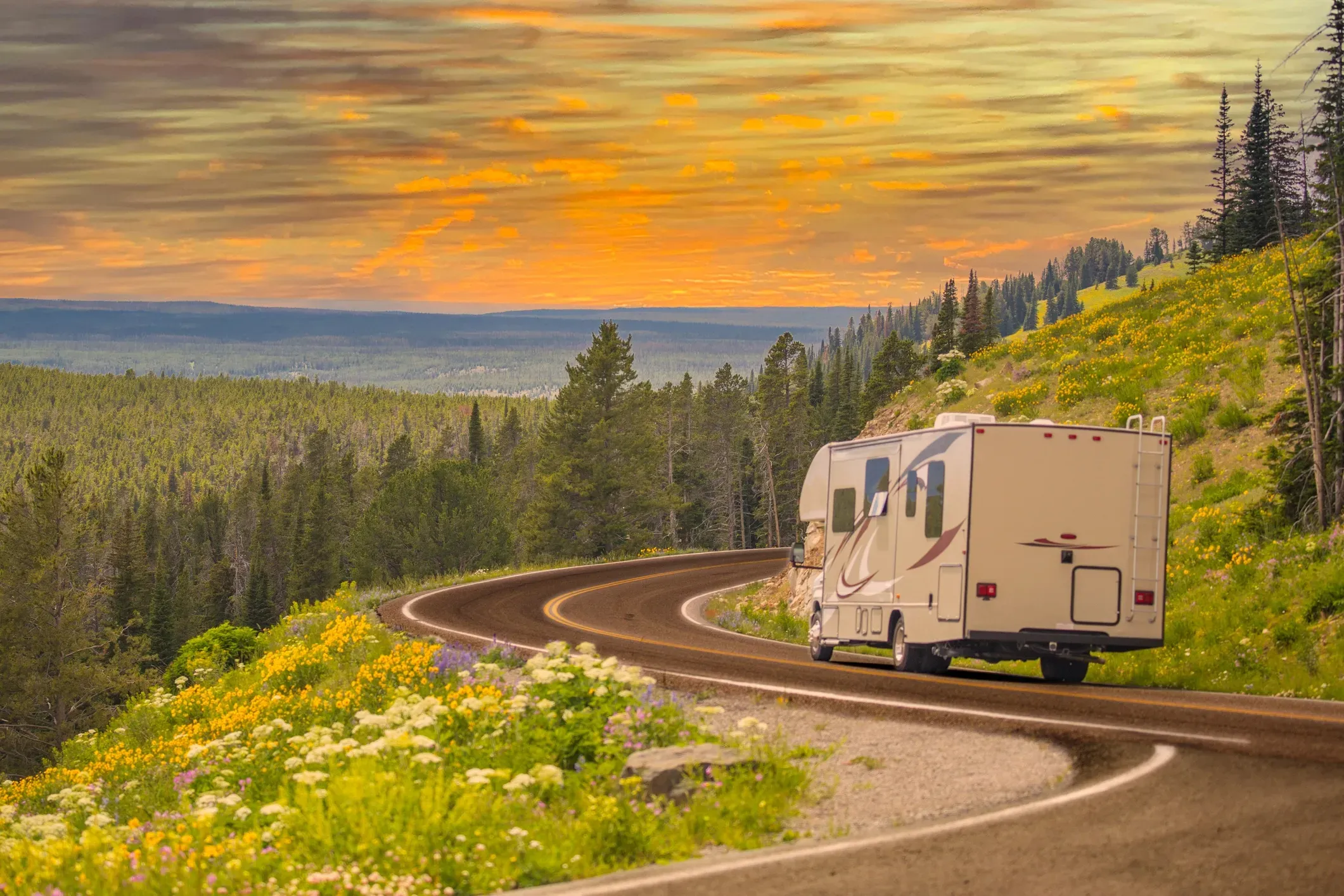 An RV driving on a winding road in the dusk with trees in the distance.