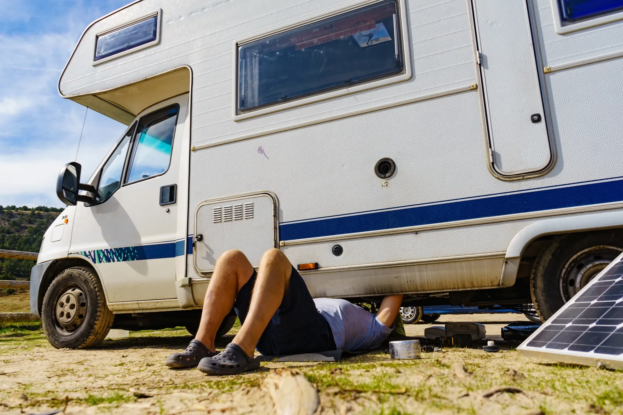 A man on his back on the ground working underneath an RV.